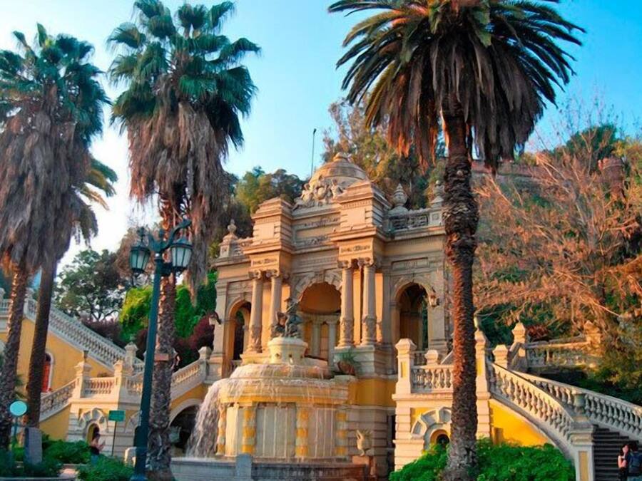 Un edificio histórico con arquitectura ornamentada, una fuente central y un puente que lo conecta.