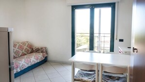 A small room with a white table, a blue-framed window, a sofa with floral upholstery, and a white chair. - SE002 - Senigallia, seafront one bedroom apartment with beach (Senigallia)