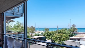 A balcony with a view of the sea, a covered outdoor seating area, and a building with a metal roof. - SE002 - Senigallia, seafront one bedroom apartment with beach (Senigallia)
