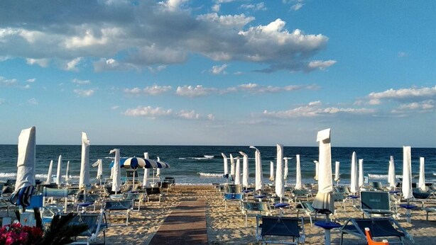 A beach with rows of sun loungers and umbrellas, a wooden walkway, and the ocean in the background. - SE002 - Senigallia, seafront one bedroom apartment with beach (Senigallia)