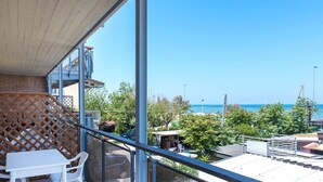 Un balcone con tavolo e sedie, affacciato su una zona costiera con alberi e cielo sereno.