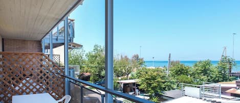 A balcony with a view of the sea, a table, chairs, and a wooden lattice.
