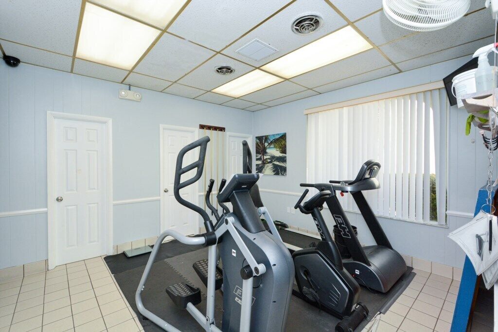 Une salle de sport équipée de matériel d’exercice, avec une porte et une fenêtre dotée de stores.