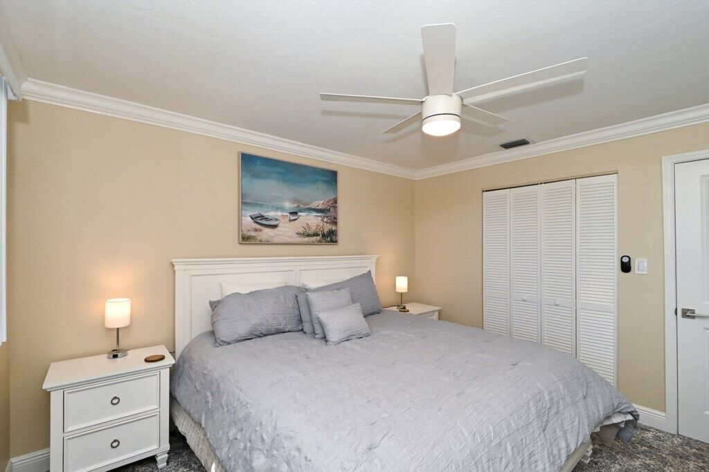 A bedroom with a bed, a nightstand, a ceiling fan, a painting, and a closet.