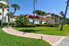 A multi-story building with a red roof, surrounded by well-maintained grass and palm trees.