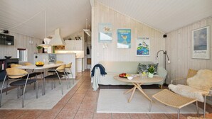 Et moderne køkken med lyse skabe, et spiseområde med et rundt bord og en hyggelig siddekrog med sofa og stole.