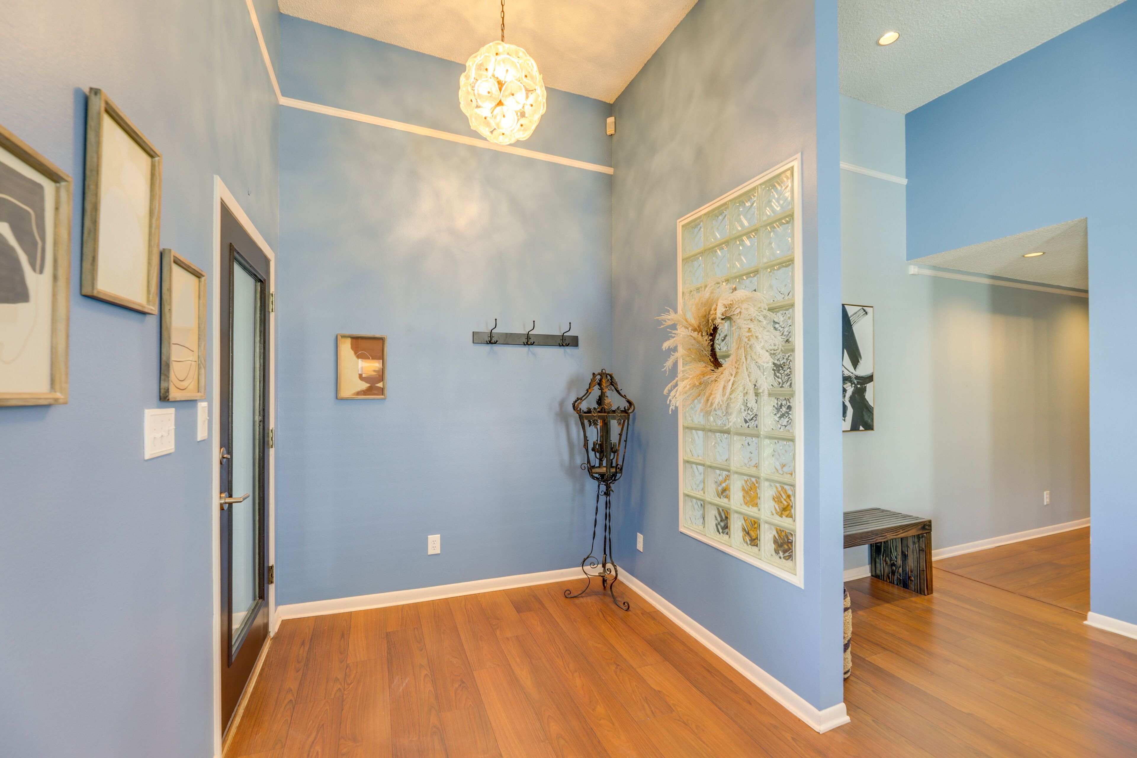A hallway with blue walls, wooden flooring, a decorative lamp, and framed artwork.