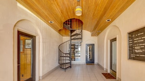 Un couloir avec un plafond en bois, un escalier en colimaçon et un panneau indiquant les noms des pièces.
