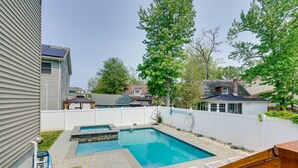 A backyard with a swimming pool, a wooden deck, and a white fence.