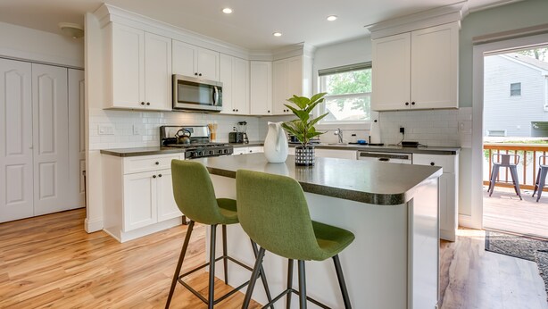 A modern kitchen with white cabinetry, a central island with green barstools, a microwave, and a large window.
