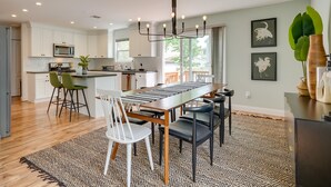 A modern kitchen with white cabinets, a central island, and a dining area with a long table and chairs.