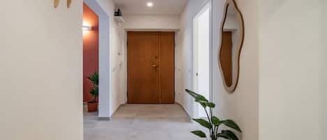 Un pasillo con una puerta de madera, una planta en maceta y un espejo en la pared.