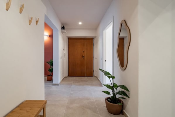 Un pasillo con una puerta de madera, una planta en maceta y un espejo en la pared.