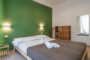 Una habitación con una cama, paredes verdes, un armario de madera y un espejo.