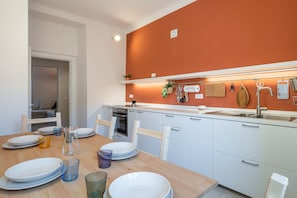 A modern kitchen with white cabinets, a wooden dining table set with plates and glasses, and a red accent wall.