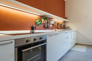 A modern kitchen with white cabinets, a stainless steel oven, and a countertop with a kettle.