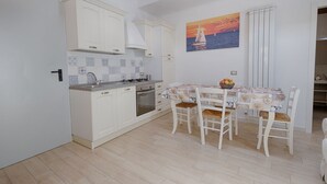 Una cocina compacta con armarios blancos, un salpicadero azulejado y un comedor con mesa y sillas.