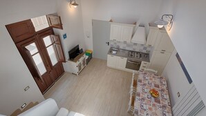 Una cocina compacta con armarios blancos, una mesa de comedor con fruteros, y una escalera que lleva a otra habitación.