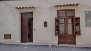 Un edificio con fachada color crema, una puerta de madera y un ventanal con persianas.