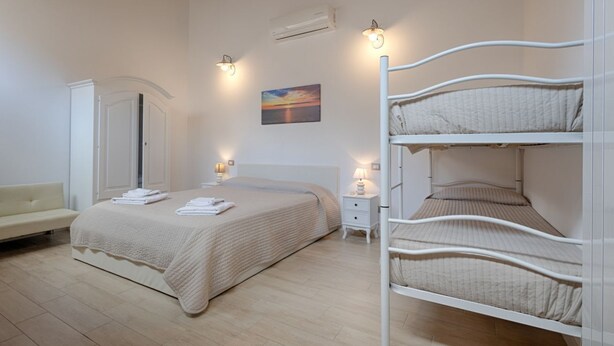 Un dormitorio con una cama individual superpuesta, una mesita de noche con lámpara, una silla y un cuadro en la pared.