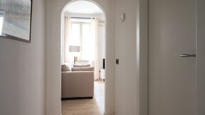 A hallway leading to a bedroom with a bed, a lamp, and a window with curtains.