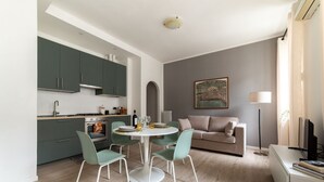A modern kitchen with green cabinets, a dining area with a round table and chairs, a sofa, and a TV.