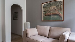 A beige sofa in a room with a framed picture of an indoor swimming pool on the wall.