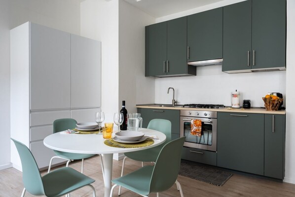 A modern kitchen with a dining area, featuring a round table, chairs, cabinets, and a stove.