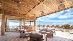 Une terrasse en bois avec des sièges extérieurs, un espace bar et une vue sur l’océan.