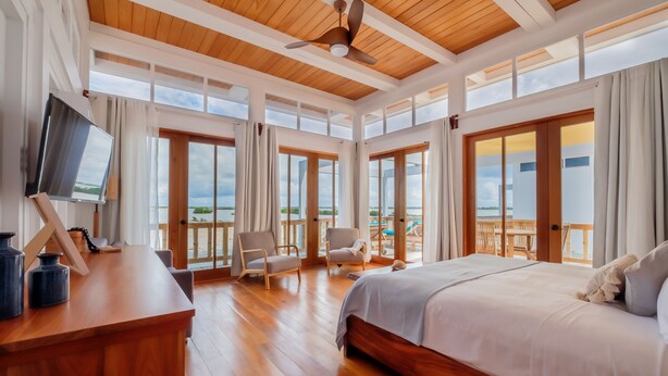 Une chambre spacieuse avec un grand lit, un plafond en bois et un balcon offrant une vue sur la mer.