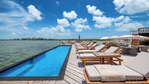 Un espace aménagé au bord de la piscine, avec des chaises longues et des parasols, donnant sur une étendue d’eau.
