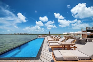 A poolside area with lounge chairs and umbrellas, overlooking a body of water. - Aruna Resort & Villas (San Pedro)