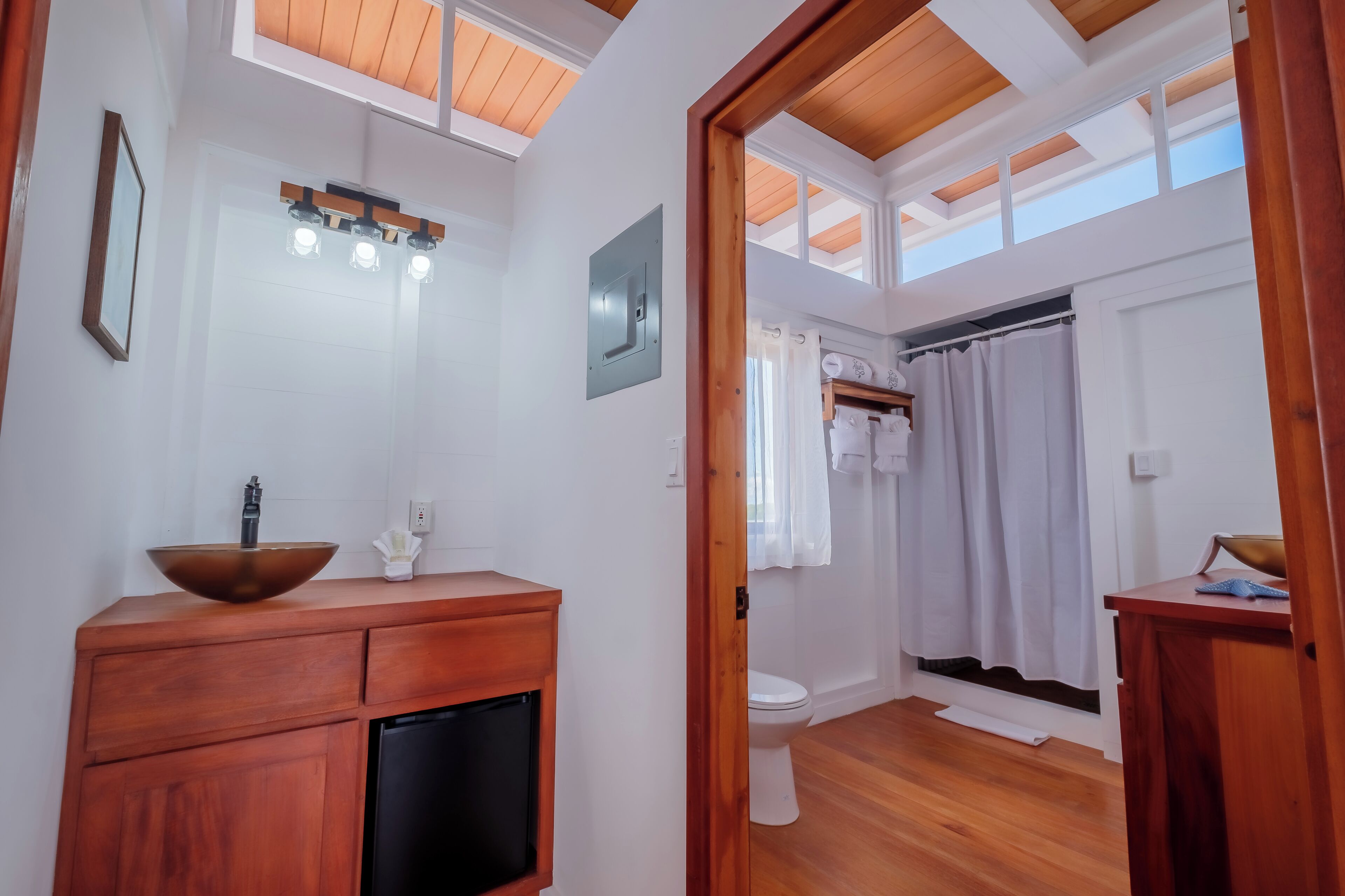 Un baño con tocador de madera, lavamanos, inodoro y cortina de ducha.