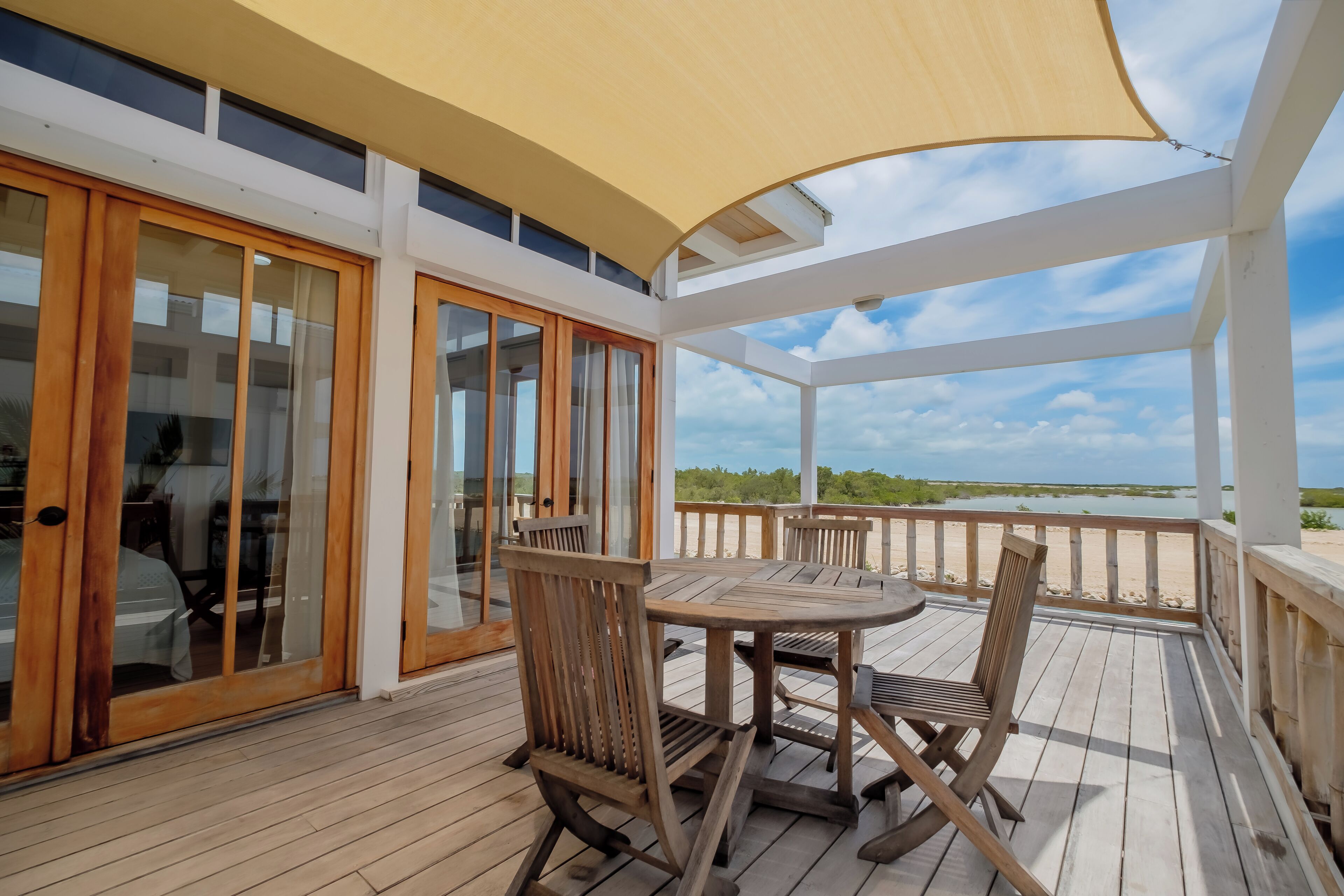 A wooden deck with a table and chairs, a covered area with a canopy, and a view of the beach.