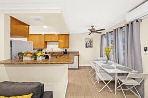 A compact kitchen with wooden cabinets, a granite countertop, and a dining area with a white table and chairs. - Cozy & Serene ~ 12 mins to Downtown LA (Alhambra)