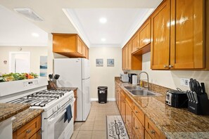 A compact kitchen with a gas stove, white refrigerator, wooden cabinets, granite countertops, and a trash bin. - Cozy & Serene ~ 12 mins to Downtown LA (Alhambra)