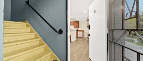 A staircase with a handrail leading to an open door, revealing a kitchen area with wooden cabinets and a dining table.