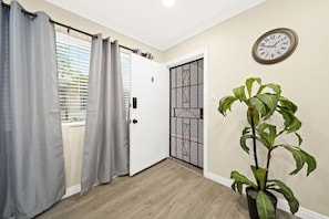 A room with a wooden floor, a white door with a metal gate, a clock on the wall, and a potted plant. - Cozy & Serene ~ 12 mins to Downtown LA (Alhambra)