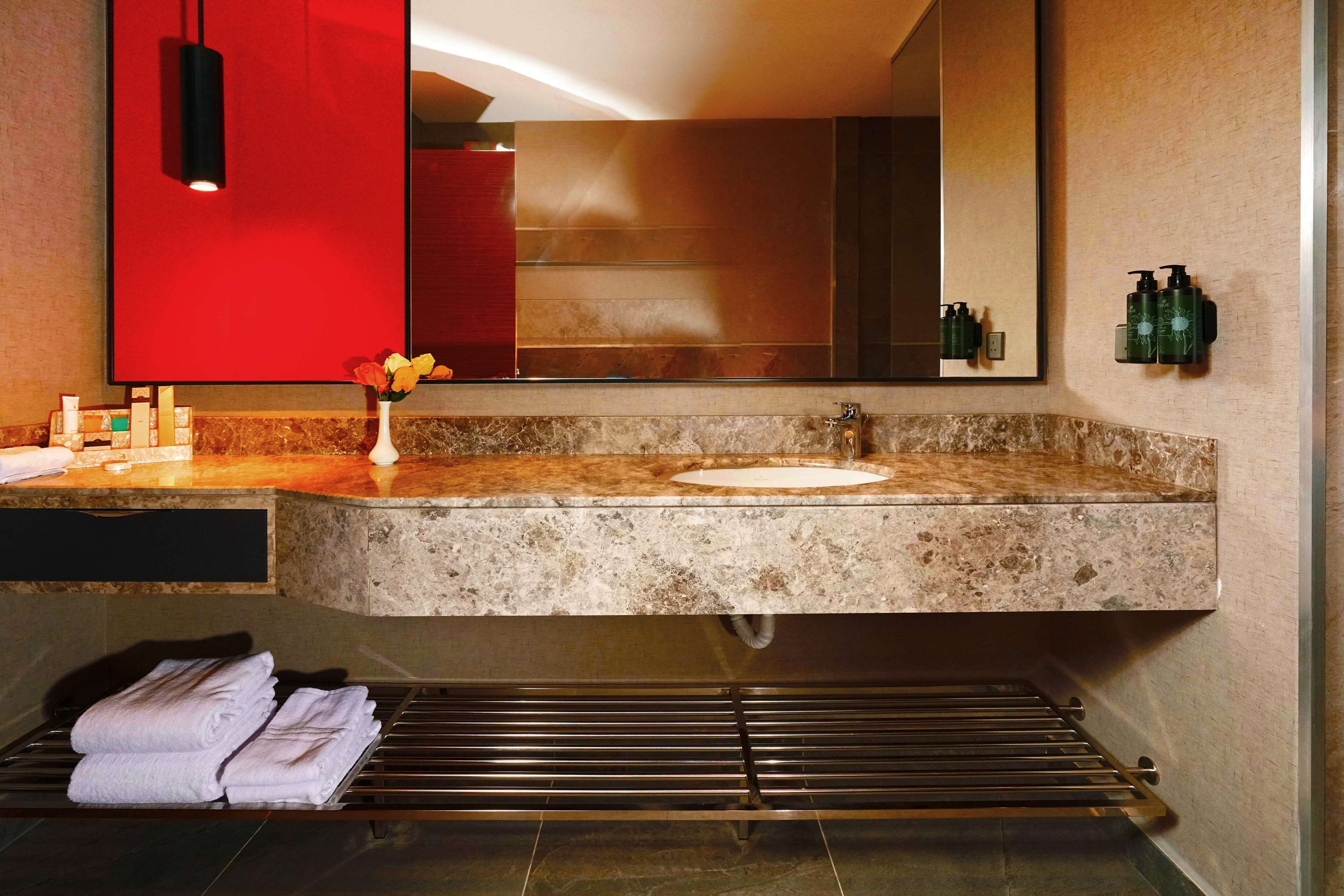 Un baño moderno con encimera de granito, un espejo grande y un perchero con toallas dobladas.