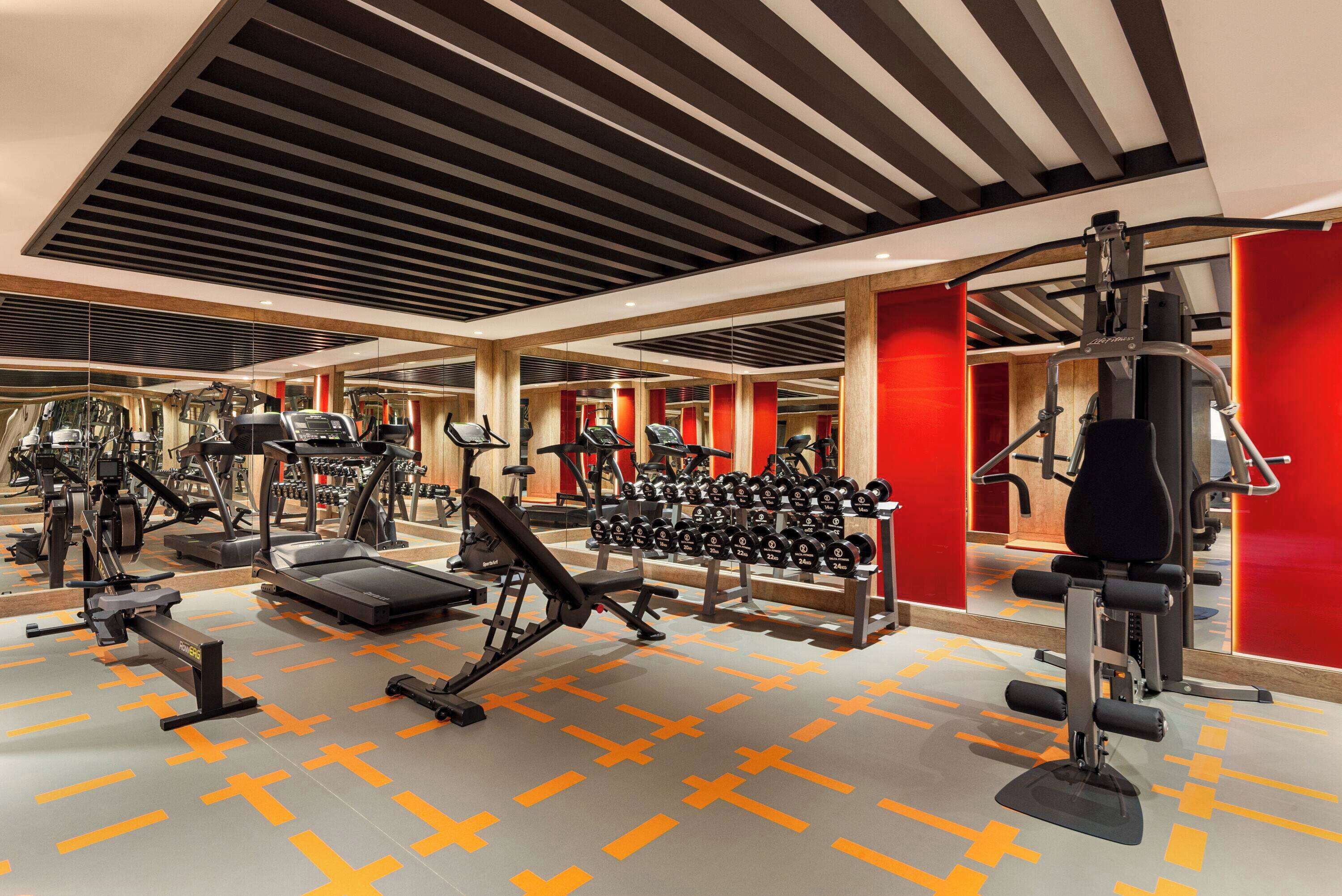 Un gimnasio con diverso equipo de ejercicio, incluyendo cintas de correr, máquinas de pesas y mancuernas.