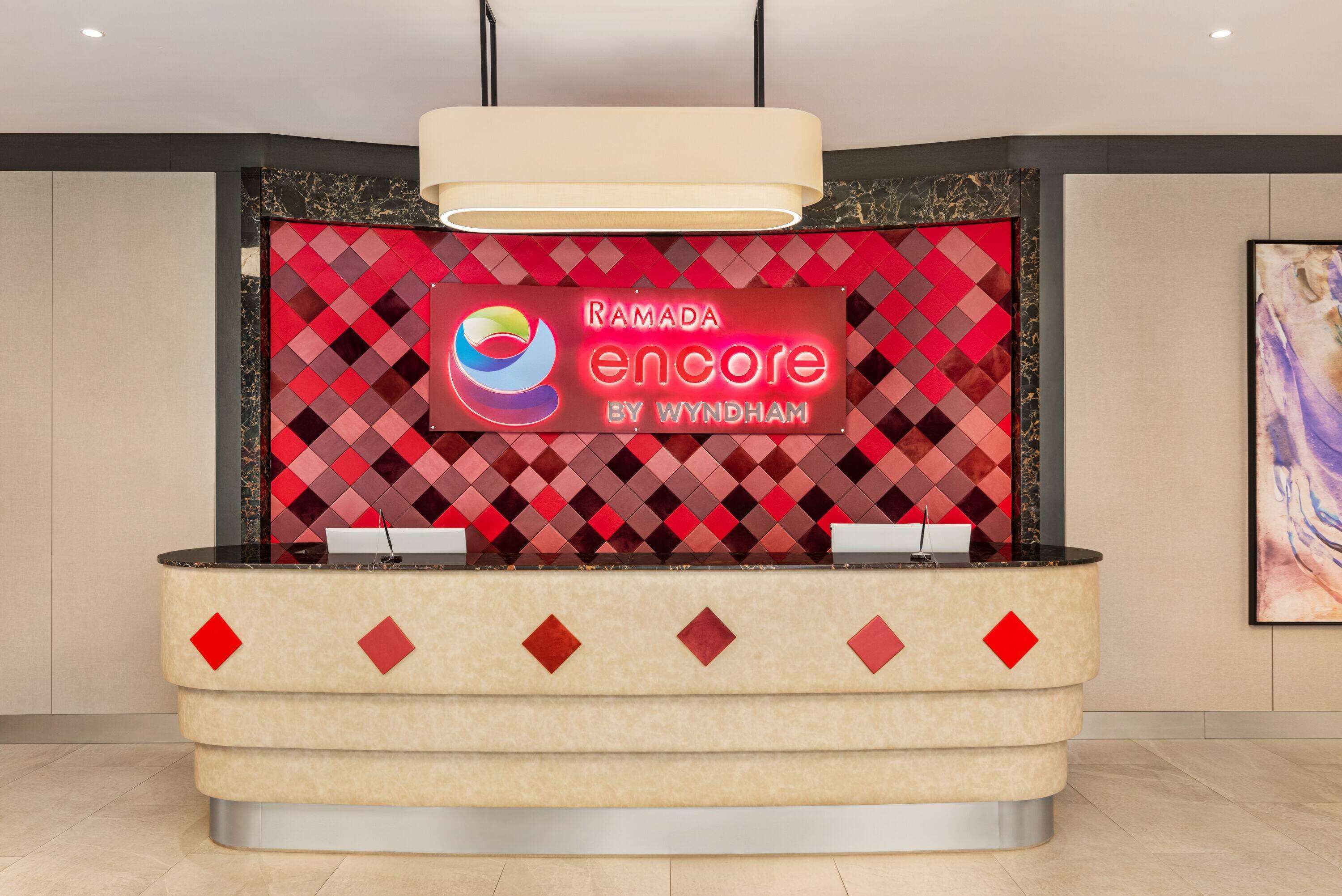 Un mostrador de recepción con un fondo de diamantes rojo y negro, un logotipo y el texto "RAMADA encore by Wyndham".