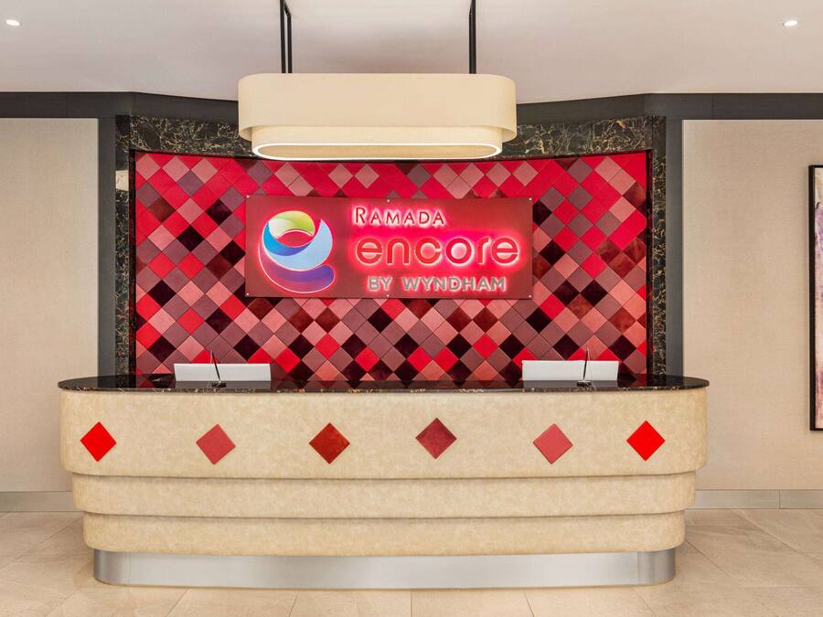 Un mostrador de recepción con un fondo de diamantes rojo y negro, un logotipo y el texto "RAMADA encore by Wyndham".
