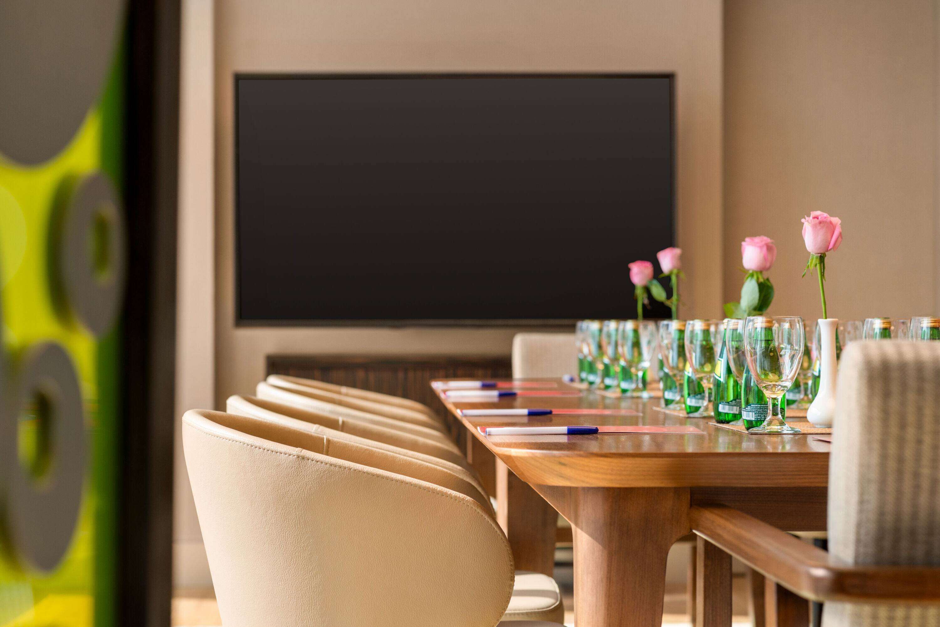 Een vergaderzaal met een lange tafel, stoelen en een groot scherm.