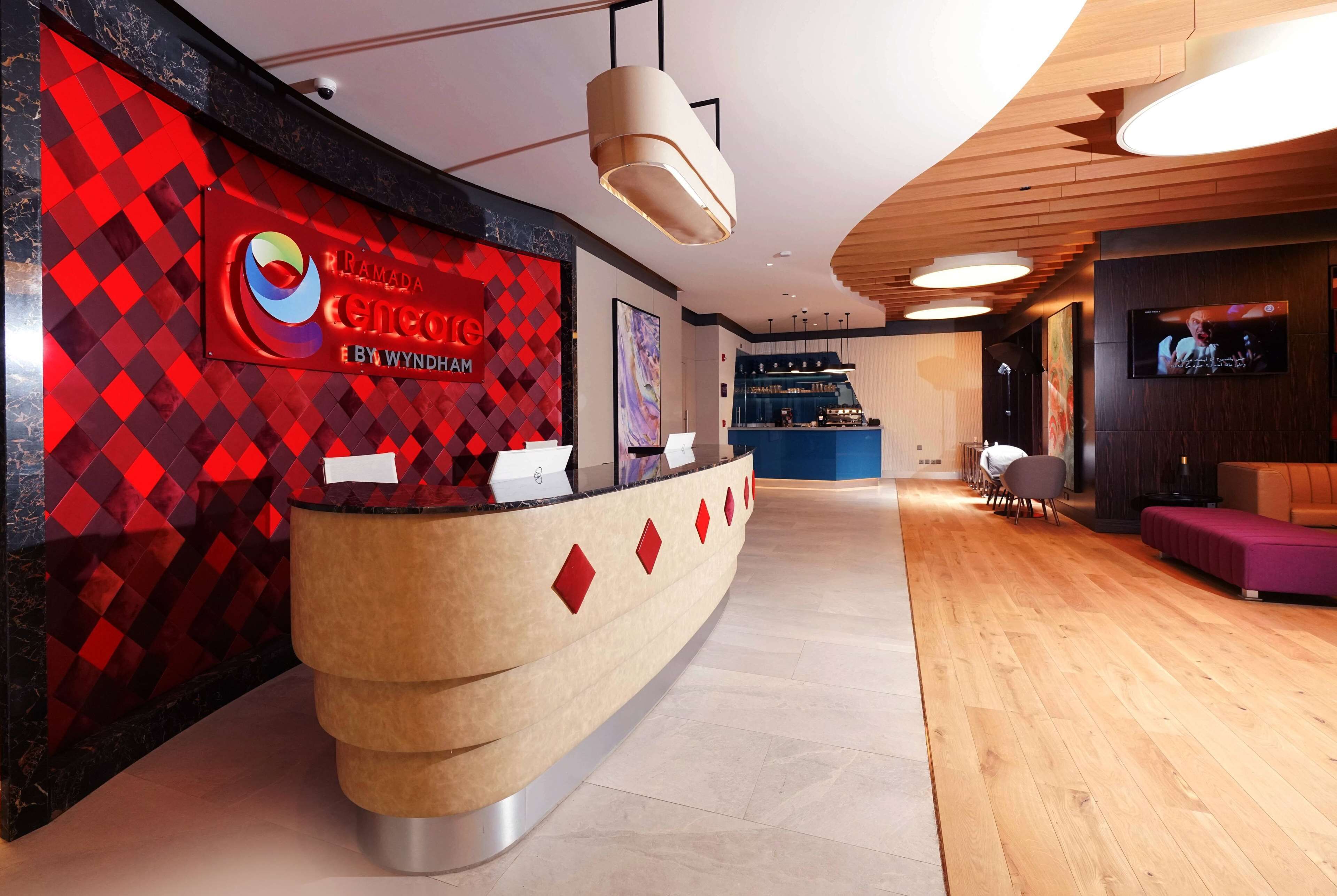 Een receptiezone met een modern design, met een gebogen receptiebalie, een scherm waarop de naam van het hotel staat, en een aan de muur bevestigde televisie.