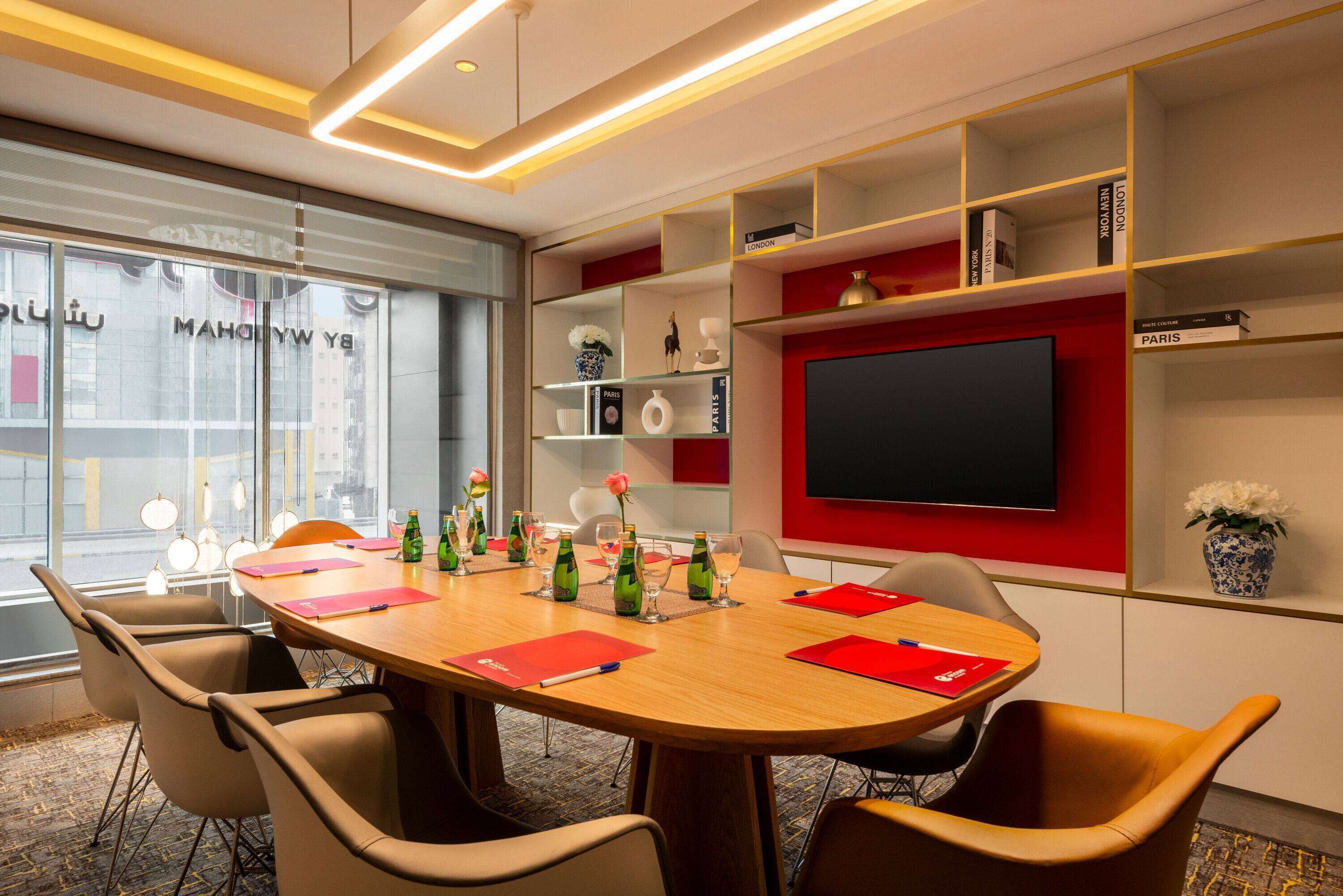 A conference room with a round table, chairs, a TV screen, and shelves with books and decorative items.