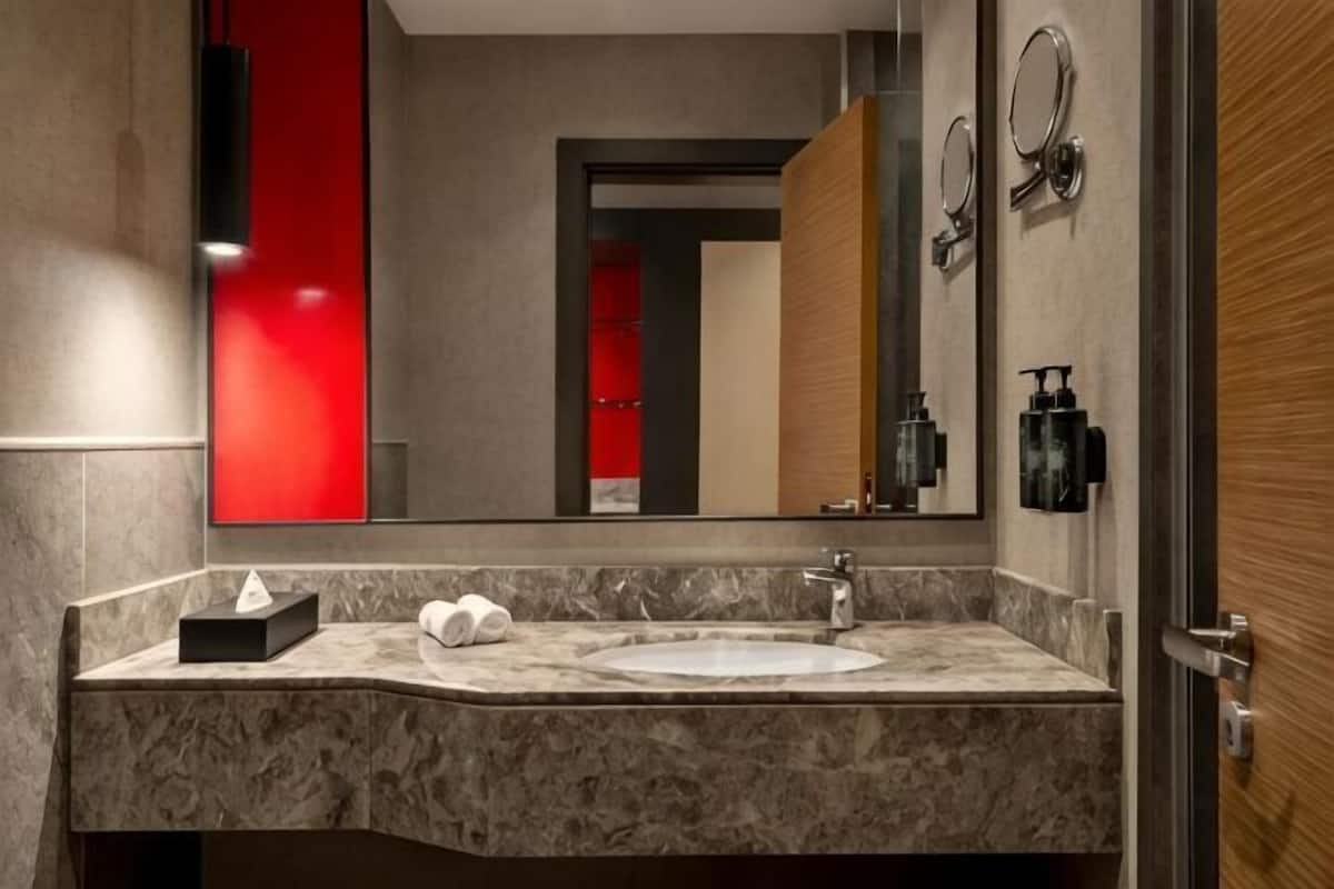 A bathroom with a marble sink, a mirror, a towel dispenser, and a red accent wall.