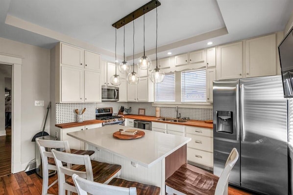A modern kitchen with white cabinetry, a central island, stainless steel appliances, and pendant lighting.