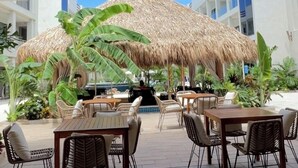 An outdoor patio with wicker furniture, a thatched umbrella, and a pool in the background.