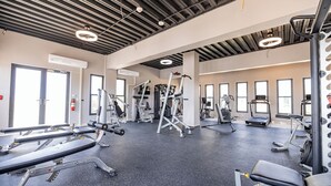 A gym with various exercise equipment, large windows, and a high ceiling with exposed beams.