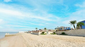 Ein Strand mit sandigem Ufer, einer Steinmauer und Gebäuden mit blauer Fassade.